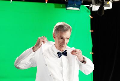 Bill Nye adjusting his lab coat on set in front of a green screen