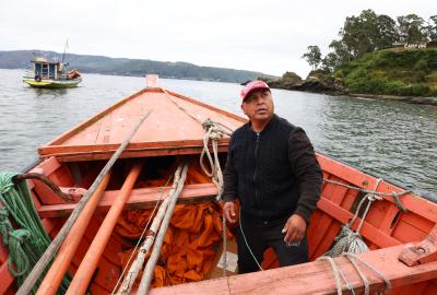 A fisher in an orange boat on their way out to fish in southern Chile