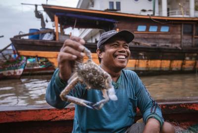 A person smiling as they hold up a crab recently caught on a small fishing boat