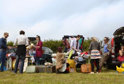 A row of people selling belongings out of the trunks of their cars