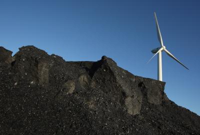 A wind turbine towering above a mound of coal