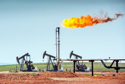 A flare of fire shoots out of an oil well with pump jacks nearby