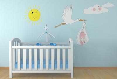 A crib with against a mural on a blue wall of a stork carrying a baby across the sky