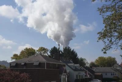 A row of suburban homes with a power plant spewing plumes of smoke directly in the background