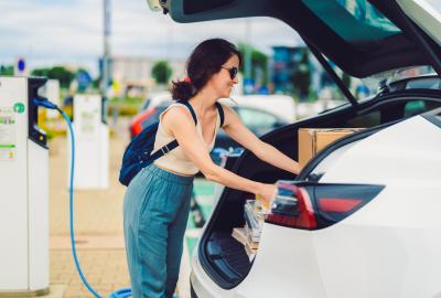 A person packing things into the trunk of an electric vehicle while it is plugged in charging