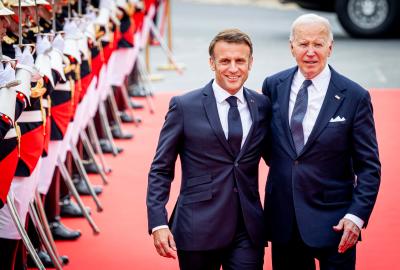 Presidents Emmanuel Macron and Joe Biden walking on a red carpet commemorating D-Day