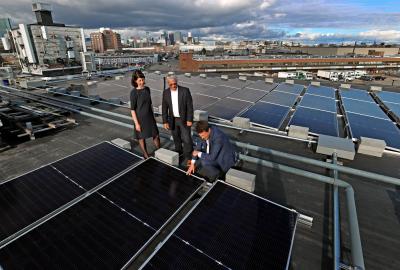 Three people standing on a rooftop looking at solar panels