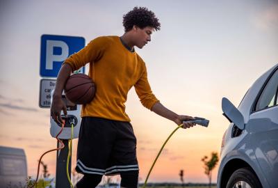 Someone plugging their electric car in while holding a basketball