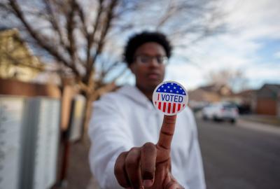A person holding up an "I voted" sticker stuck to their finger