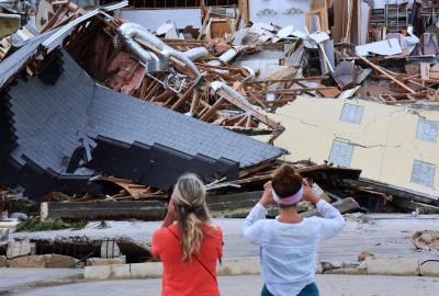 Two people taking photos of destroyed houses after a natural disaster