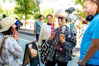 A woman wearing recycled items as a hat, including soda cans hanging down at a street fair during New York City Climate Week