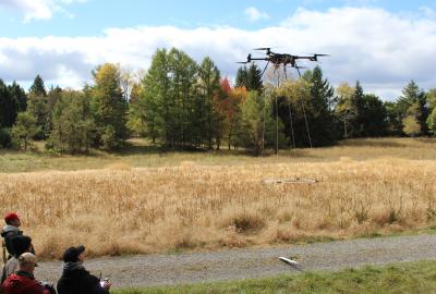 A group of onlookers watch a drone lifting into the sky