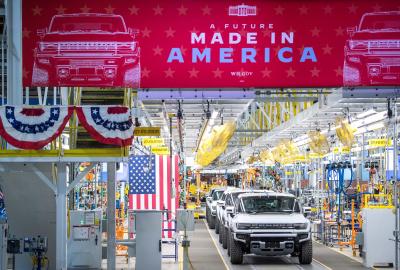 Electric vehicles on a manufacturing line with American flags on the sides and a banner that reads "Made in America" above the assembly line