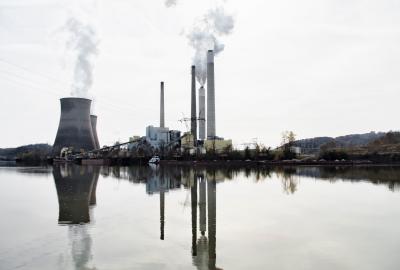 A power plant belching smoke and steam next to a reflective lake