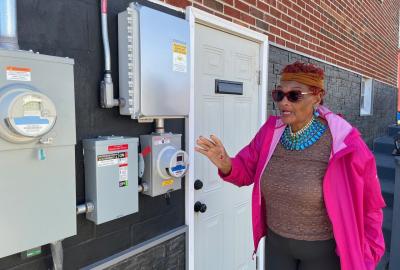 Mary West standing outside of her house pointing to the electric meter