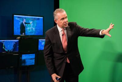 John Morales standing in front of a greenscreen doing the weather