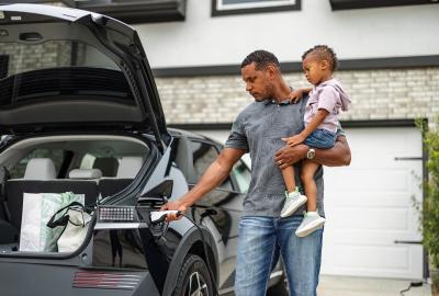 A dad holding a kid while plugging in an electric vehicle