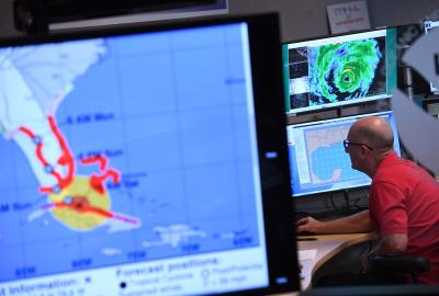A man in the background working at a computer with weather information in the foreground