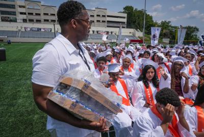 A man handing out bottles of water to high schoolers at their graduation 