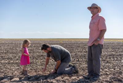 Dwane Roth standing next to his nephew Zion as he digs in the soil. His daughter is standing next to him in a pink dress