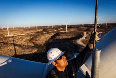 A person wearing a safety helmet and gloves working on top of a wind turbine structure