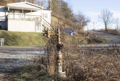 A rusty pipe sticking out of the ground with a house and car in the near background