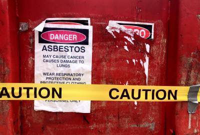 A sign that reads "Danger Asbestos" stuck to a red door with caution tape in front of it