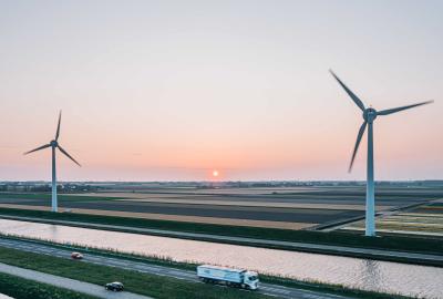 A truck driving on the foreground and large wind turbines in the background