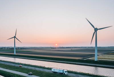 A truck driving on the foreground and large wind turbines in the background