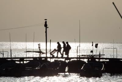 Fishers walking across a wharf with the sun behind them 