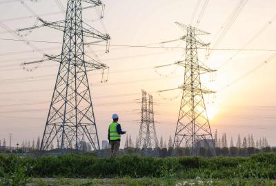 A worker looking up at towering electrical lines and transmission towers