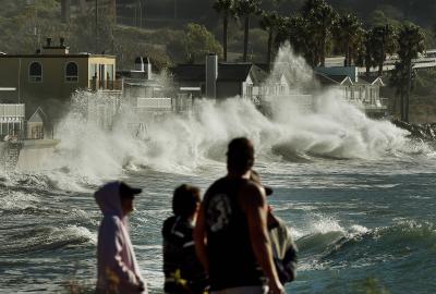 Huge waves crashing in the background with people looking on in the foreground