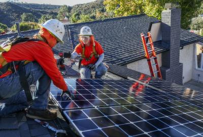 Two people installing a solar panel on a rooftop