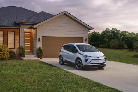 Chevrolet bolt electric car parked in front of a brightly lit home at dusk