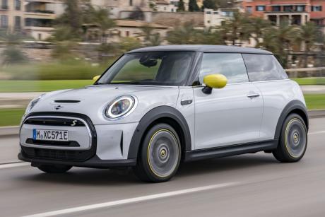Silver and black mini electric hardtop car driving in front of blurred city background