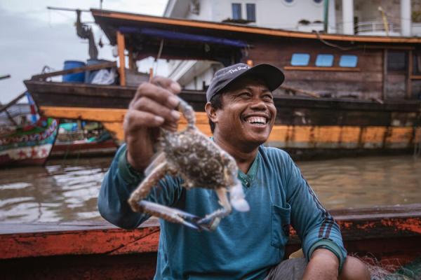 A person smiling as they hold up a crab recently caught on a small fishing boat