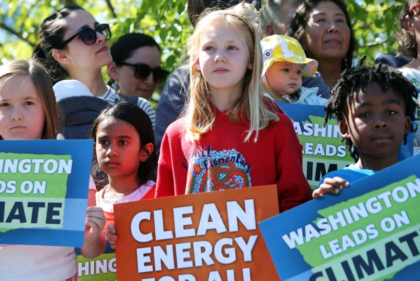 A young girl standing center among other kids holding signs that say "Clean energy for all" and "Washington leads on climate"