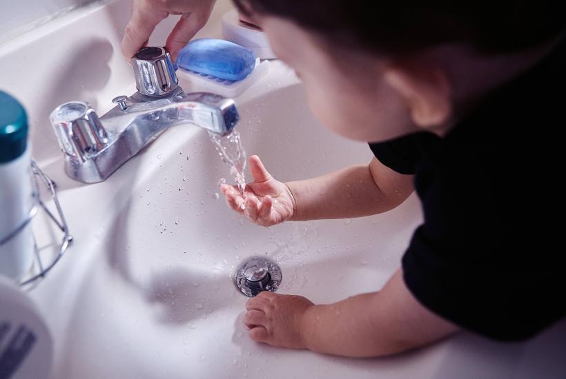 A baby washing their hands in a bathroom sink