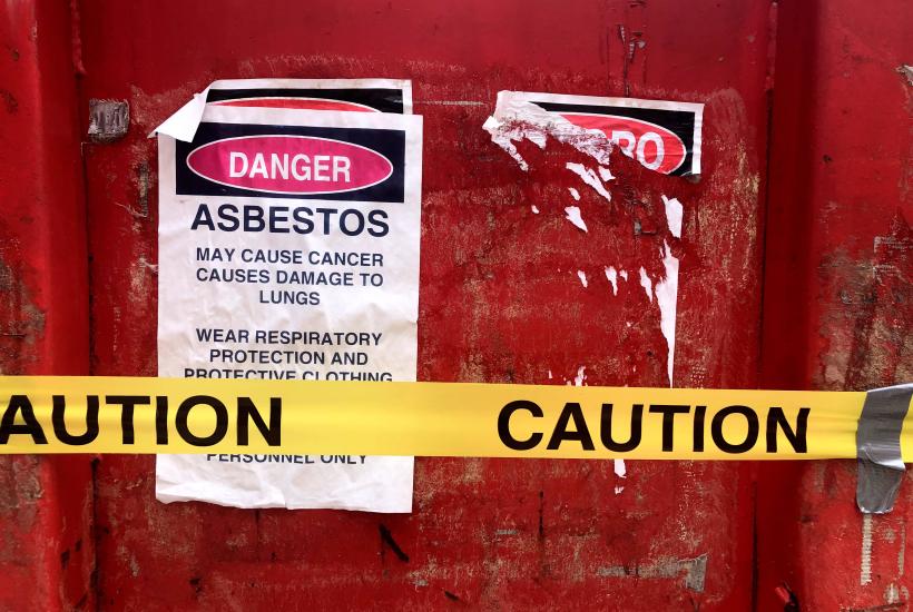 A sign that reads "Danger Asbestos" stuck to a red door with caution tape in front of it