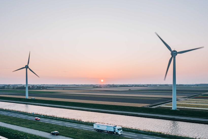 A truck driving on the foreground and large wind turbines in the background